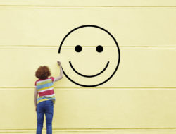 Girl drawing smiley face on to a wall