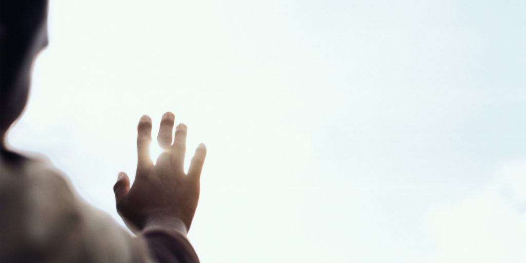 Young man blocking sun with hand, close up